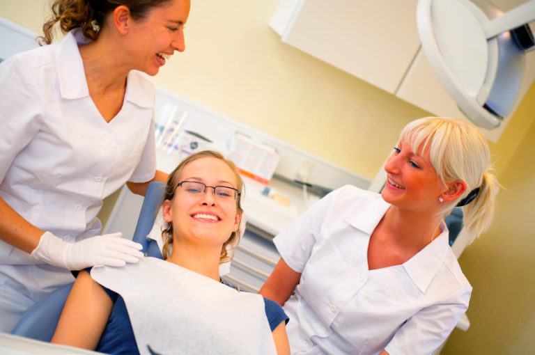 A dentist and dental hygienist smiling at their patient in the dental chair