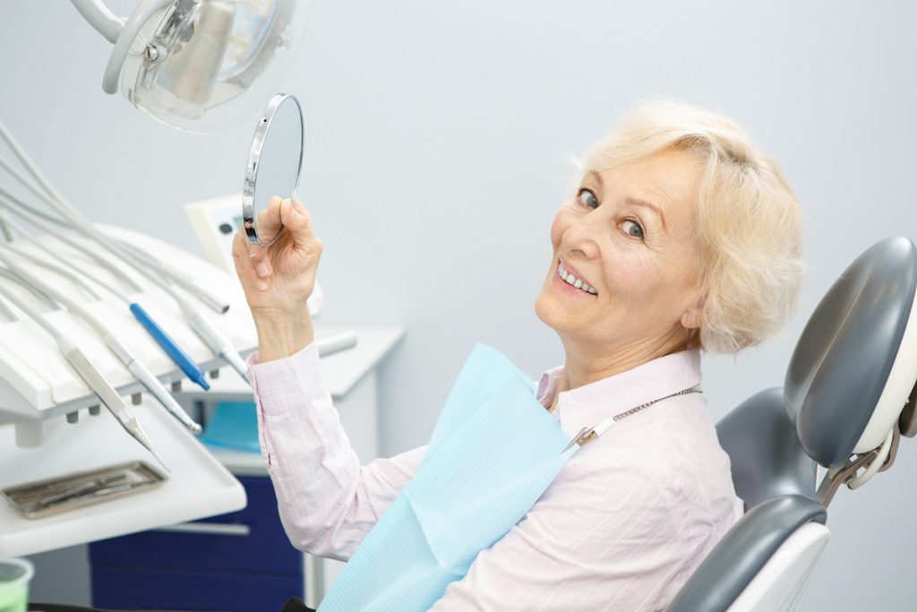 A patient at Cobblestone Park Family Dental admiring her dentures